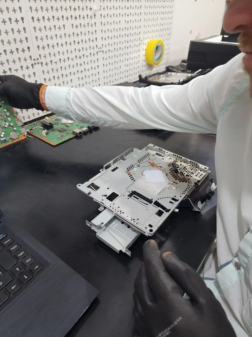 Técnico com luvas desmontando um console na bancada